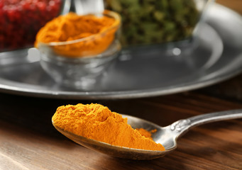Spoon with turmeric powder on wooden table, closeup