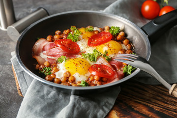 Fried eggs with bacon and chickpeas in pan on table