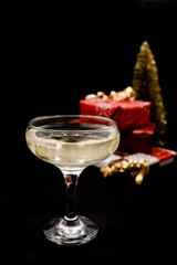 A glass of champagne with bubbles. Christmas presents and a goldn pine tree on dark black background.