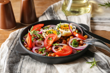 Delicious fried chickpeas with eggs and vegetables in pan on table