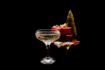 A glass of champagne with bubbles. Christmas presents and a goldn pine tree on dark black background.