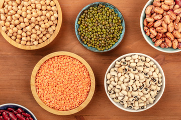 A photo of various types of legumes, shot from the top on a dark rustic wooden background....