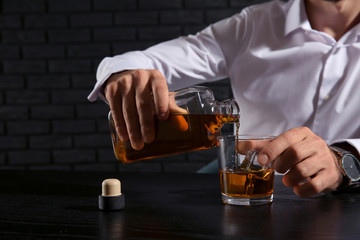 Man pouring whiskey into glass while sitting at table on dark background