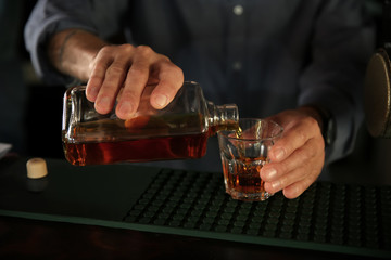 Barman pouring whiskey into glass in pub, closeup