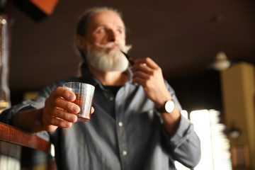 Senior man with glass of whiskey and pipe in pub