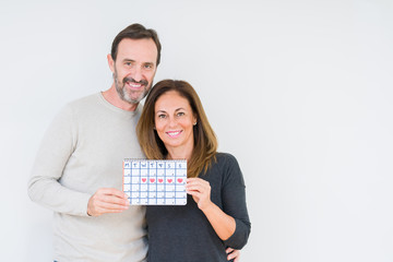 Middle age couple holding month calendar over isolated background with a happy face standing and smiling with a confident smile showing teeth