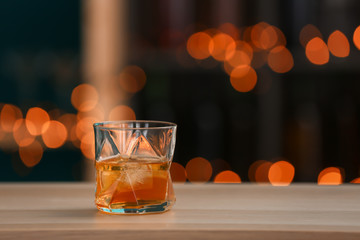 Glass of whiskey on wooden table against blurred lights