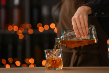 Female bartender pouring whiskey from bottle into glass on table