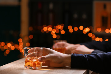 Man with glass of whiskey at wooden table in bar