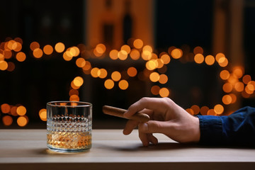 Man with glass of whiskey and cigar at wooden table in bar
