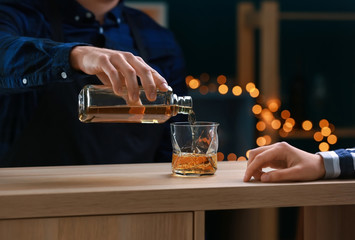 Male bartender pouring whiskey from bottle into glass in bar