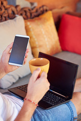 Man using cellphone and laptop while drinking coffee / tea on the porch.