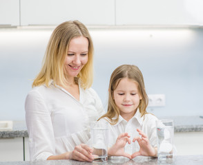 Little girl with a glass of water and happy mother at kitchen