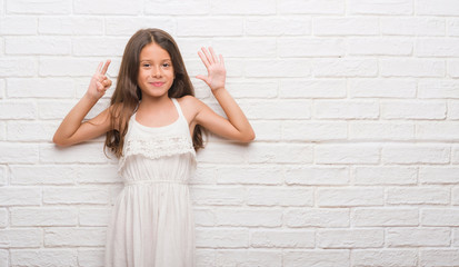 Young hispanic kid over white brick wall showing and pointing up with fingers number seven while smiling confident and happy.