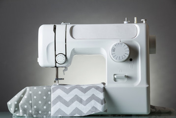 White modern electric sewing machine on gray background and fabric cuts
