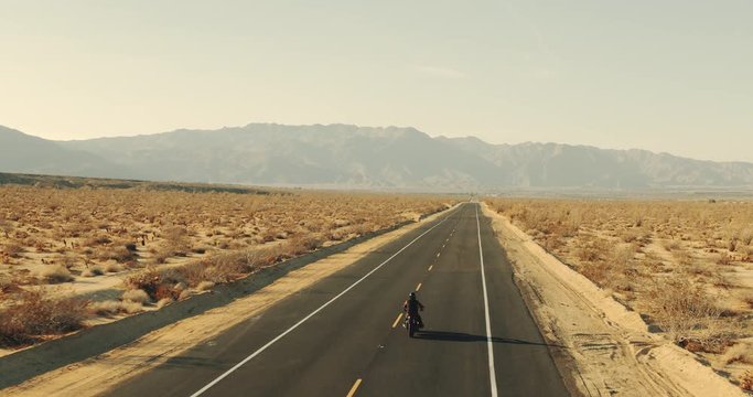 Aerial view of man riding motorcycle down desert road at sunset 