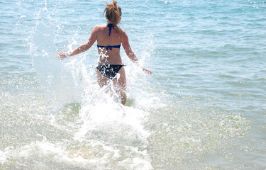 The girl at the resort, from the beach runs into the water with splashes during the holidays.