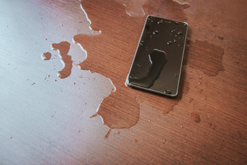 Smartphone wet by accident on wooden table.