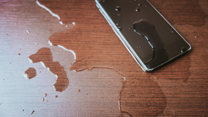 Smartphone wet by accident on wooden table.