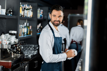 smiling handsome bartender polishing glass at workplace