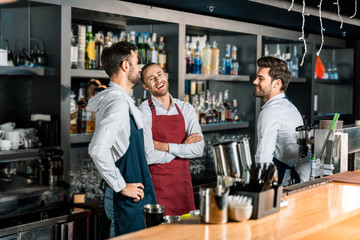 cheerful happy handsome barmen in aprons talking at workplace