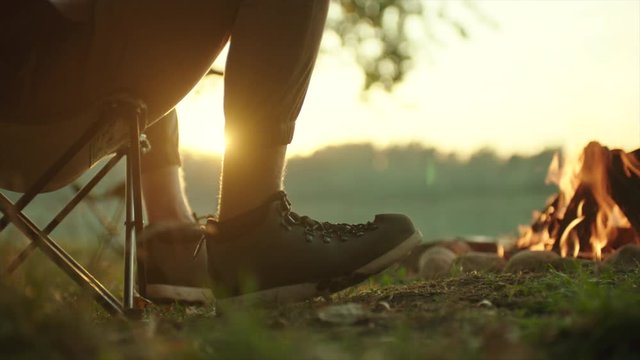 Close up of hikers feet in trekking boots near bonfire at sunset