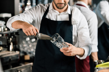 cropped view of  barman in apron putting ice in glass with ice shovel