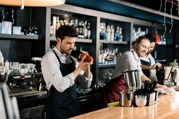 adult barman in apron shaking cocktail in glass with shaker