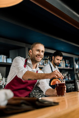 handsome smiling bartender serving cocktail at wooden counter