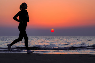 Alone woman running on sand beach. Beautiful red sunset. Enjoying sport in evening. Copy space. Empty place for motivational, inspirational text, quote or sayings on sky background. Side view.