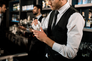 Bartender cleaning glass with white cloth in bar