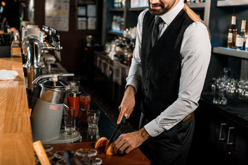 Barman slicing fruit on cutting board in bar