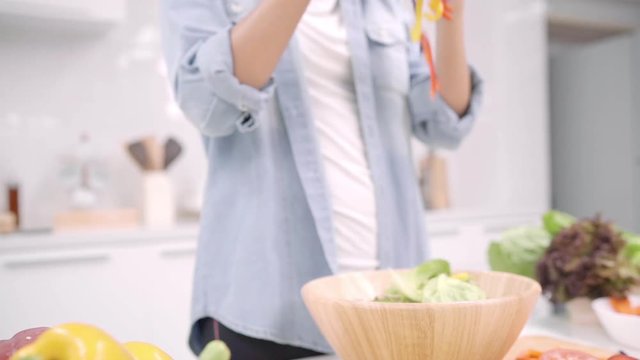 Slow motion - Young Asian woman making salad healthy food in the kitchen, beautiful female in casual use organic vegetables lots of nutrition preparing salad for fit body at home. Healthy food concept