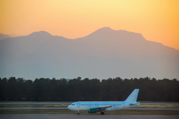 Airplane on the runway in the background of mountains with sunset
