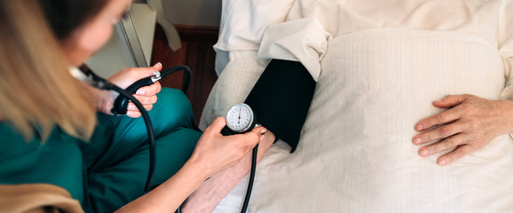 Unrecognizable female caregiver checking blood pressure to a senior woman at home