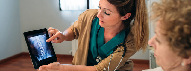 Female doctor showing to female senior patient an x-ray on the tablet