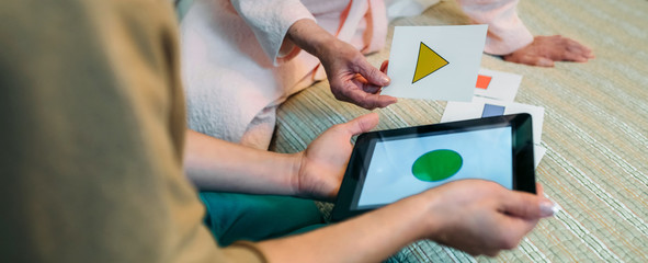 Female doctor showing geometric shape game to elderly female patient with dementia
