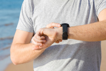 Young man using smart watch for running on sea beach. Checking heart rate before and after workout. Monitoring of daily health with modern devices. Front view of body part. Closeup.
