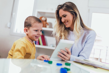Young mother and her son play in kids room. Funny mom and lovely child are having fun with tablet.
