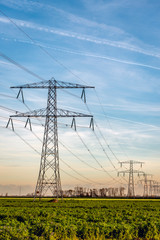 High voltage pylons with cables in a long row in a rural landscape in the Netherlands