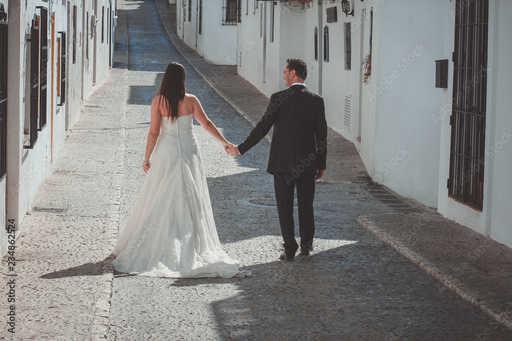 Wall mural bride and groom walking along the street in a mediterranean village