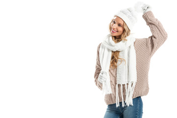 Cheerful young woman in beige knitted sweater, white hat, mittens and scarf smiling isolated on white