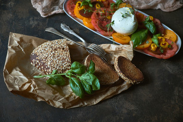 Still life in dark tones of farm bread and salad of fresh vegetables and mozzarella. Still life in a rustic style. Healthy and environmentally friendly food. Farm products. Healthy lifestyle.