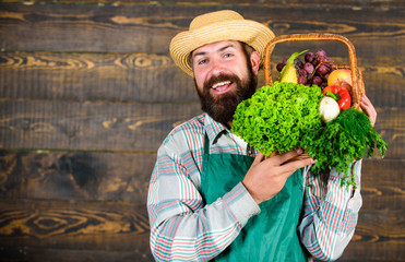 Farmer straw hat deliver fresh vegetables. Farmer with homegrown vegetables in basket. Man bearded farmer presenting eco vegetables wooden background. Fresh organic vegetables in wicker basket