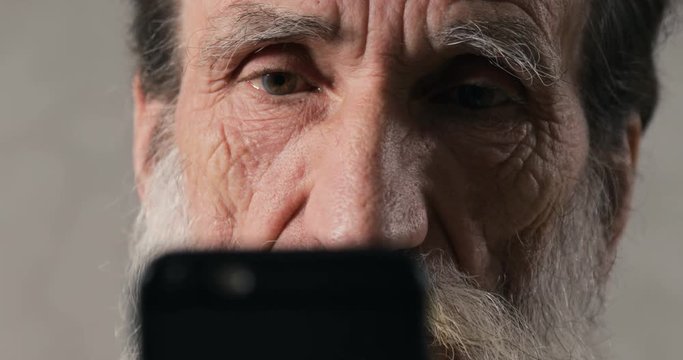 Senior man is shocked when using new black smartphone, spending time with gadget at warm sweet home, closeup