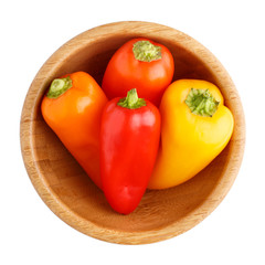 Red, orange and yellow bell peppers in wooden bowl isolated on white background. Top view.