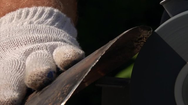 Sharpening of soiled and rusty garden tool with unbalanced grinding machine in slow motion close up. Panning of traditional machinery scene with detailed round-pointed steel shovel and waving hand