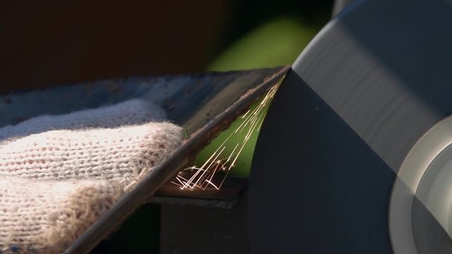 Sharpening of soiled garden tool with unbalanced grinding machine in slow motion close up. Panning of traditional machinery scene with detailed round-pointed steel shovel, waving hand in safety glove.
