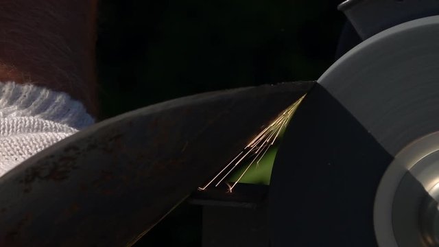 Sharpening of soiled and rusty garden tool with unbalanced grinding machine in slow motion close up. Panning of traditional machinery scene with detailed round-pointed steel shovel and waving hand