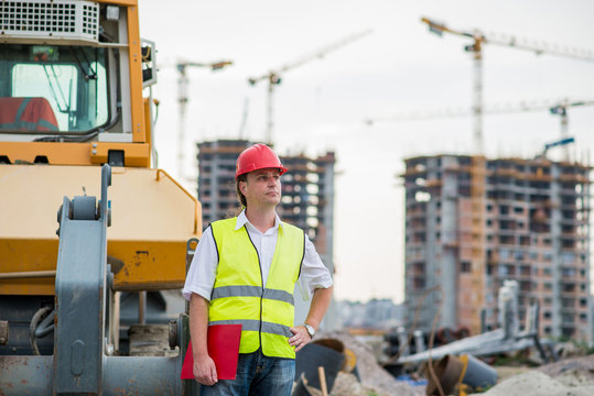 Engineer in front of excavator on a construction site with buildings and cranes in the background